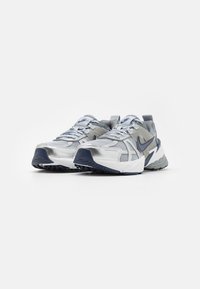Nike running shoes featuring a silver mesh upper, dark blue accents, textured sole, and reflective details. Design is athletic with a robust shape.