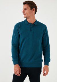 Tyrkysový polo s dlhým rukávom, s golierom, trojbuttonovou légou a stočenými manžetami. Mäkká textúra a priliehavý strih.
