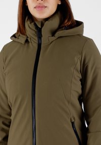 Giacca softshell verde oliva con colletto alto, zip frontale completa e dettagli delle cuciture sottili. Leggera con una finitura texture.