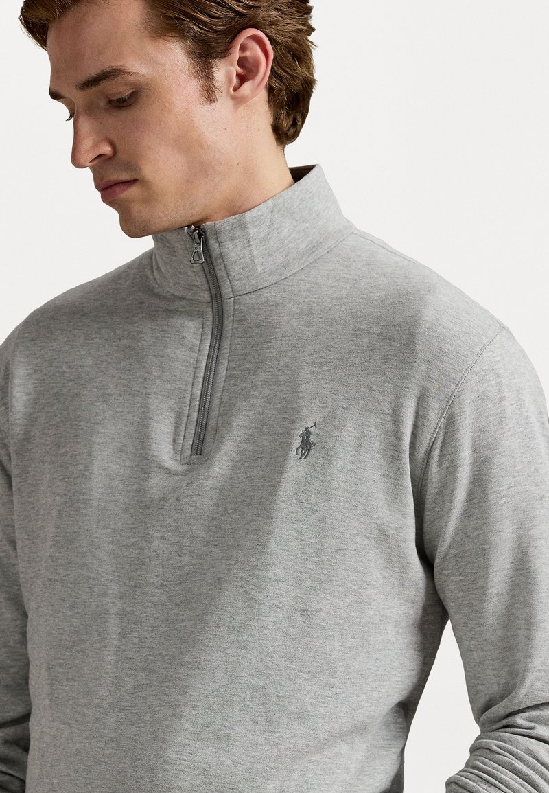 Sudadera de media cremallera en color gris, fabricada en un tejido suave, con un pequeño logotipo bordado en el lado izquierdo del pecho y un acabado suave.
