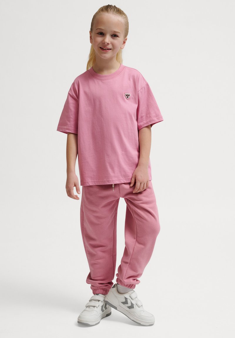 Rosa Baumwoll-T-Shirt mit kleinem Blumenmotiv, kombiniert mit rosa Sweatpants mit elastischen Bündchen; getragen mit weißen Sportschuhen.