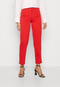 Pantalon rouge ajusté à coupe slim, fabriqué en tissu lisse. Associé à une chemise blanche à col et des talons noirs à brides.