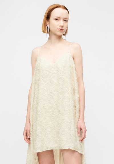 Φόρεμα σατέν σε κρεμ απόχρωση με λεπτό υφή, ντεκολτέ σε σχήμα V και λεπτές τιράντες· διαθέτει μακρύτερο πίσω μέρος για μια αέρινη σιλουέτα.