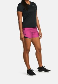 Zwart atletisch topje met korte mouwen gecombineerd met roze short met een zwarte tailleband. Draagt zwarte sneakers met een gestructureerd patroon.