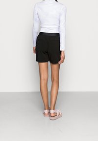 Zwarte shorts met een relaxed fit, gecombineerd met een strakke witte lange mouwtop. Lichtroze sandalen met zichtbare banden op de voeten.