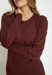 Burgundy knit sweater with ribbed cuffs and a round neckline, featuring a soft texture and slight puff at the shoulder seams.