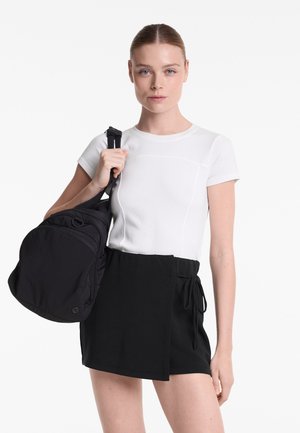 Vitt kortärmat linne med texturerad tyg och svarta högmidjade shorts med sidoknyt, parat med en svart ryggsäck.