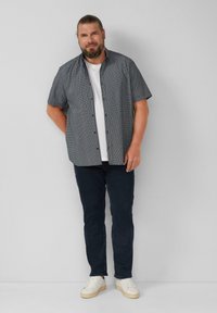 Korte mouwen overhemd met een patroon in marineblauw en wit, gecombineerd met een wit T-shirt, donkere spijkerbroek en witte sneakers.