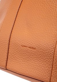 Tan leather bag featuring a textured finish, vertical seam lines, and embossed "GERRY WEBER" logo. Compact and rectangular shape.