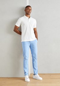 Bijela kratkodlaka polo majica, svijetloplave slim-fit chinos hlače i bijele tenisice. Minimalistički dizajn, glatka tekstura i moderni kroj.
