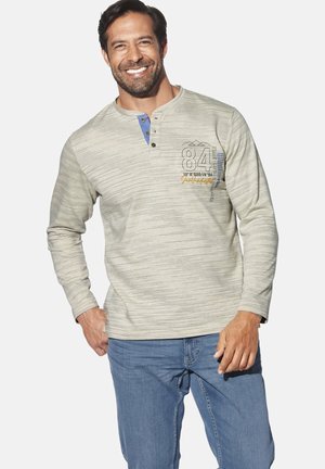 Hellgraues Langarmshirt mit horizontalen Streifen, blauer Knopfleiste und Druckgrafik auf der Brust. Kombiniert mit blauen Jeans.