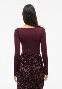 Bordeaux longsleeve top met een bootnek, gecombineerd met een met pailletten versierde rok die textuurpatronen en een aansluitend ontwerp benadrukt.