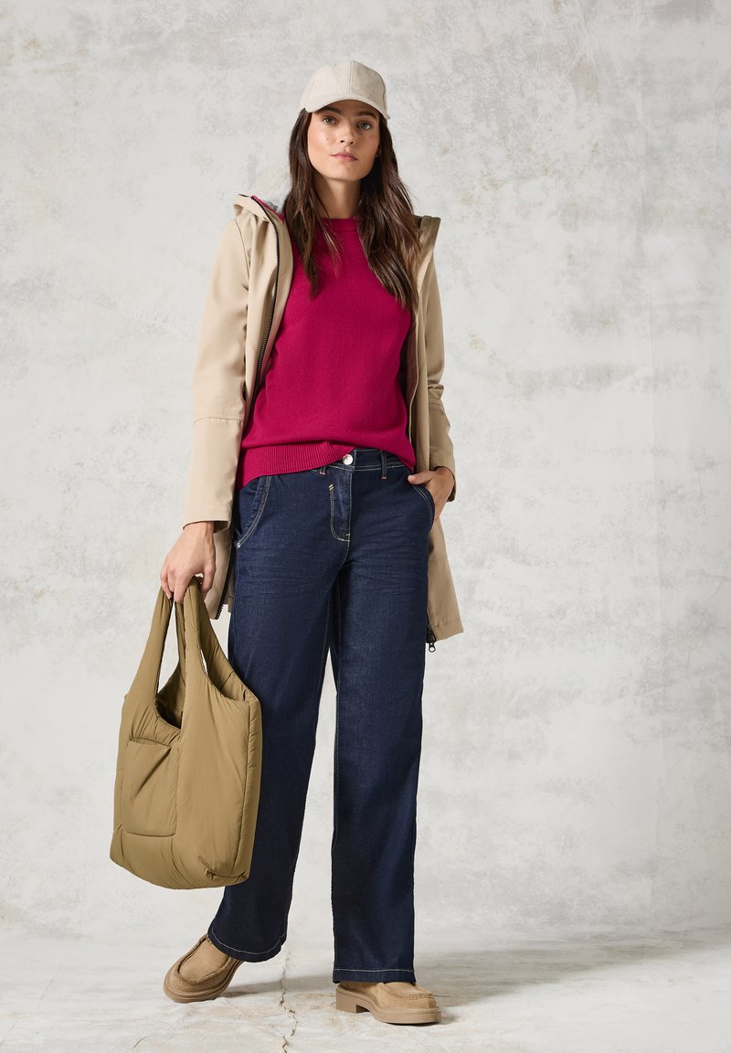 Beige wasserdichte Jacke, fuchsia Pullover, dunkelblaue weit geschnittene Jeans, hellbraune Knöchelstiefel und eine hellbraune Schultertasche mit einer Tasche.