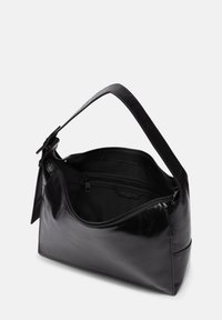 Bolso de mano de cuero negro con textura lisa, forma curvada, una sola correa y compartimento con cremallera que revela un forro negro.