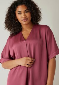 Blusa ampia a scollo a V in raso rosa antico. Presenta maniche corte e una caduta delicata, con una superficie liscia e senza motivi visibili.