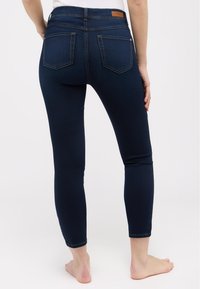 Skinny jeans in dark blue denim, featuring a high waistband, two back pockets, and minimal stitching details. Flat, smooth fabric texture.