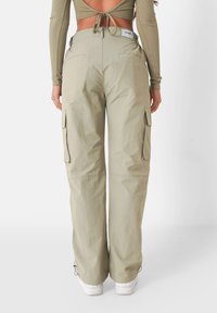 Lichtgroene cargobroek met een hoge taille, zijzakken en elastische boorden bij de enkels. Gemaakt van een lichtgewicht, gladde stof.