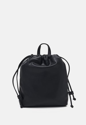 Sac en cuir lisse noir à cordon avec une poignée supérieure et des cordons latéraux réglables sur un fond clair uni.