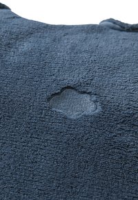 Nahaufnahme eines dunkelblauen Stoffes mit einem Riss, der das darunter liegende hellere blaue Material zeigt.