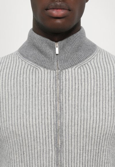 Grau gerippter Strickpullover mit hohem Kragen und Reißverschluss. Weiche Textur und auffällige vertikale Streifen, mit glänzendem Metallreißverschluss.