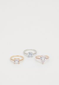 Tres anillos en exhibición: uno de plata con una piedra redonda, uno de oro rosa con una piedra rectangular y uno de oro rosa con una piedra en forma de pera, todos con piedras de acento.