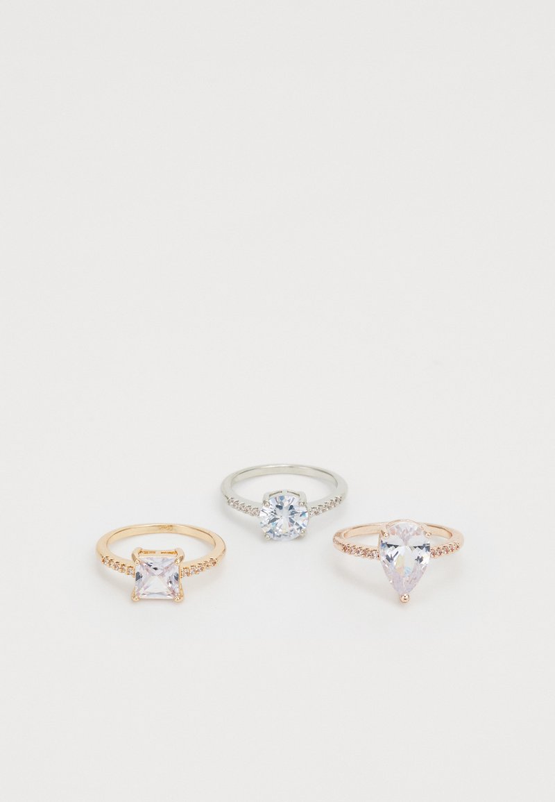 Tres anillos en exhibición: uno de plata con una piedra redonda, uno de oro rosa con una piedra rectangular y uno de oro rosa con una piedra en forma de pera, todos con piedras de acento.