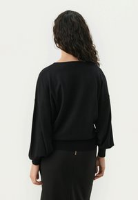 Maglione nero a maglia con spalle scese, maniche ampie e vestibilità rilassata. Texture a coste all'orlo e ai polsi, superficie liscia.