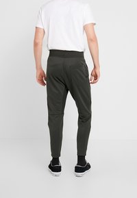 Men's dark green jogger pants with a tapered fit, elastic waistband, and back pocket details. Made of a smooth, stretchy fabric.