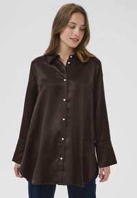Brown satin long-sleeve shirt with a placket of white buttons, pointed collar, and flared cuffs, featuring a curved hem and smooth texture.