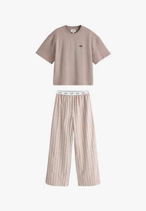 Person wearing a loose brown t-shirt with "self." printed and a striped skirt, hand tucked into the skirt pocket.