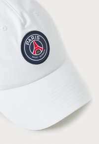 Biela baseballová čiapka s kruhovým vyšívaným logom s červenými a modrými akcentmi, na prednej strane je text "PARÍŽ" a "SAINT-GERMAIN".