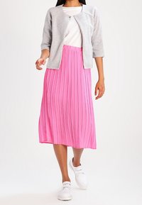 Gray, textured cardigan over a white top, paired with a pleated, mid-length pink skirt. Worn with white sneakers.