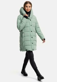 Mint green puffer coat with a large, foldable hood, snap buttons, and diagonal stitching. Worn over black pants and boots.