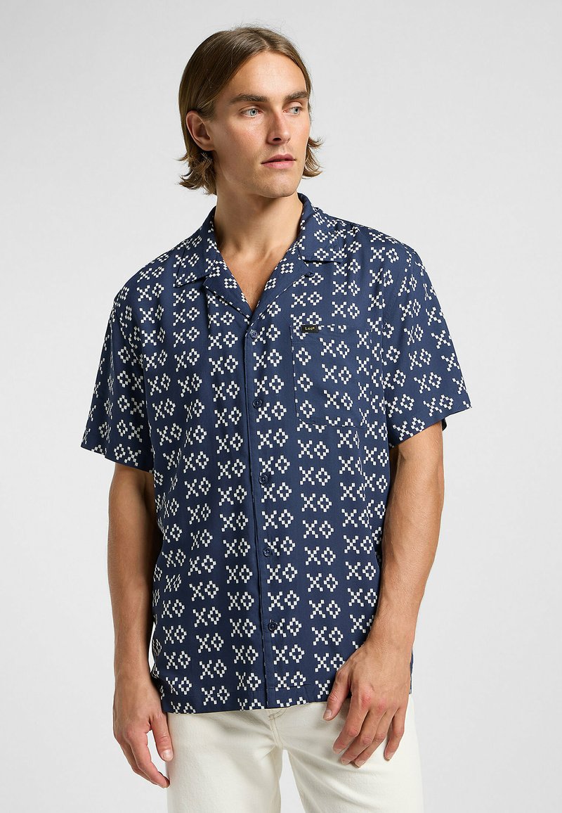Chemise à manches courtes bleu marine, ornée d'un motif géométrique blanc. Poche unique sur la poitrine. Tissu doux avec une coupe décontractée.