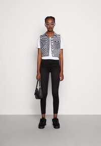 Colete recortado em xadrez preto e branco por cima de uma t-shirt branca, combinado com jeans skinny pretos e ténis pretos de sola grossa. Pequena bolsa preta.