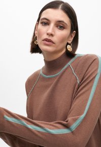 Hnědý rolák se světle tyrkysovými akcenty na ramenou a rukávech, s jemnou texturou a žebrovanými manžetami.
