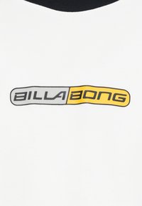 Tricou alb cu mâneci scurte și guler rotund negru, cu un logo "BILLA BONG" gri și galben într-un font modern în centrul acestuia.