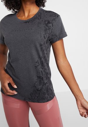 Kvinde iført en mørkegrå kortærmet skjorte med teksten "REBELLION" og et subtilt slangemønster, kombineret med høj taljede pink leggings.