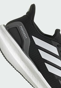 Botte de sport noire avec tige en mesh, design à trois bandes blanches et semelle texturée. Présente des détails 'Pureboost' sur le côté.