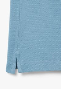 Light blue textured fabric with a side slit and seam detail, likely the lower hem of a garment.