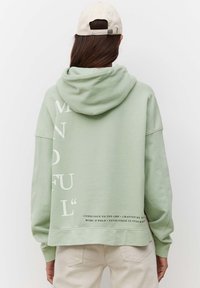 Sudadera verde claro con un bolsillo tipo canguro, corte holgado y un gran texto gráfico blanco en la parte posterior. Cuenta con capucha y puños acanalados.