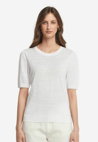 Hvid strikket kortærmet sweater med rund halsudskæring, ribbede manchetter og kant. Stoffet har en let, let gennemsigtig tekstur.