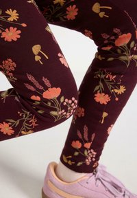 Leggings i mørk bourgogne med et blomster mønster, der indeholder orange og guld blomster, svampe og grønne blade. Blødt, strækbart stof.