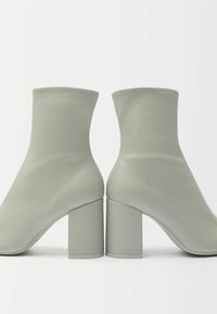 Szare botki na kostkę z gładką syntetyczną cholewką, elastycznym wałem i masywnymi obcasami. Charakteryzują się minimalistycznym designem oraz bezszwową konstrukcją.