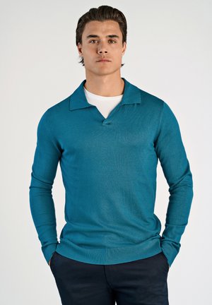 Suéter de punto teal con escote en V y amplio cuello, que cuenta con mangas largas y dobladillo acanalado, usado sobre una camisa blanca.