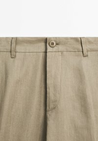 Beige lněné kalhoty s předním zapínáním na knoflík, rovného střihu a jednou zakřivenou boční kapsou s jemnou texturou.