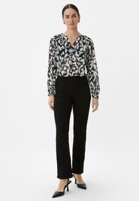 Multikleurige blouse met abstract patroon in zwart, wit en lichtblauw, gecombineerd met zwarte strakke broek en zwarte puntige hakken.