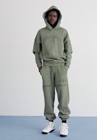Ensemble de sweat à capuche vert olive et pantalon assorti, en tissu mélangé coton, coupe décontractée, poignets côtelés, poche kangourou, baskets blanches.