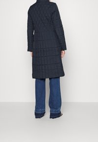 Abrigo largo acolchado en azul marino, con cuello alto y mangas largas. Silueta en línea A con un tejido liso y texturizado.