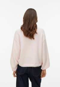 Mīksts rozā džemperis no pūkaina materiāla, ar saīsinātu dizainu, platiem piedurknēm un vienkāršu apmali. Valkāts kopā ar tumšām džinsa biksēm.